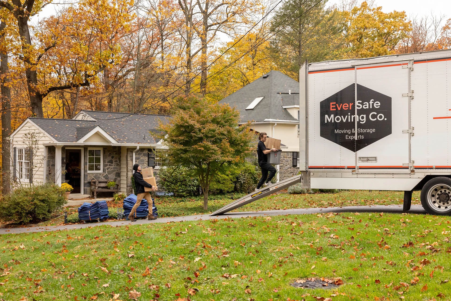 Movers loading boxes into an EverSafe Moving Co. truck outside a suburban home in autumn