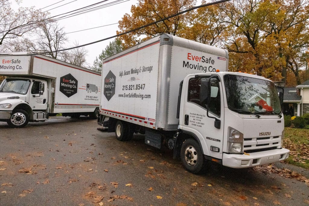 Two EverSafe Moving Co. trucks are parked curbside in a leafy residential neighborhood