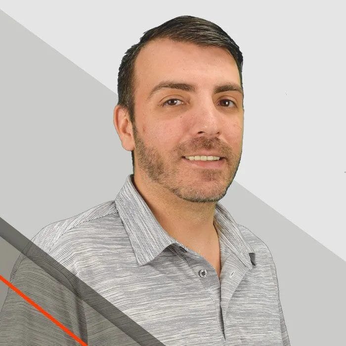 Jay, Managing Partner, wearing a striped polo shirt stands in front of a gray and white background
