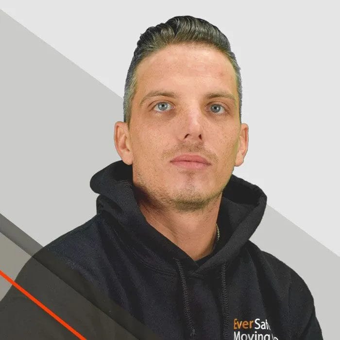 Tim, Mover, wearing a black hoodie looks forward with a calm, confident expression