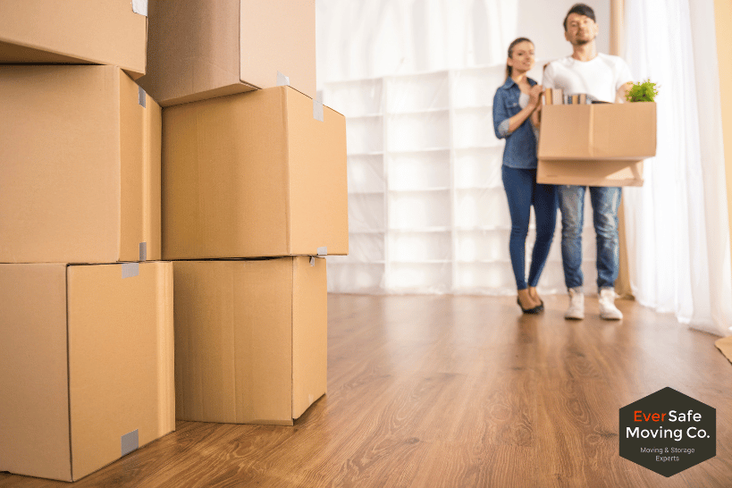 Couple carrying moving boxes with more boxes placed on the floor